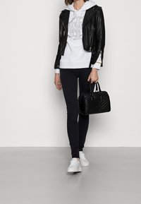 Giubbotto da biker in pelle nera sopra una felpa bianca con cappuccio, abbinato a jeans skinny neri e sneakers bianche. La borsa è nera con dettagli trapuntati.