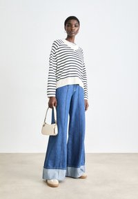 Pull rayé à manches longues en blanc et marine, associé à un jean en denim bleu à jambes larges avec un ourlet replié, et un petit sac à main crème.