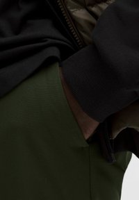 Mustmust värvi puuvillane sviiter ribitud varrukatega, koos tumeroheliste kangast pükstega. Keskenduge tasku piirkonnale ja kihilistele tekstuuridele.