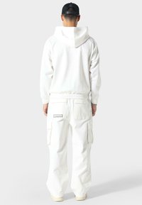 Felpa bianca con orlo elastico e dettaglio del logo sul retro, abbinata a pantaloni cargo bianchi coordinati con tasche laterali e una toppa sul retro.