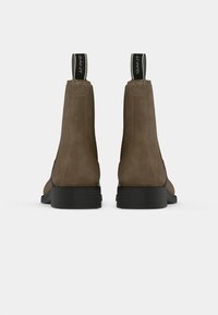 Des bottines en daim marron à talons bas noirs, avec une languette et des détails en couture simples sur le dessus.