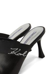 Czarne skórzane klapki z eleganckim otwartym tyłem, z logo "Karl" w kolorze srebrnym na pasku i smukłym obcasem. Gładka powierzchnia.