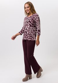 Langärmliges Oberteil mit burgunderfarbenem und weißem Tierdruck, kombiniert mit dunkelbordeauxfarbenen Hosen und taupefarbenden Blockabsatz-Stiefeletten.