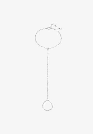 Anillo de cadena de plata con eslabones delicados, que presenta pequeñas piedras preciosas. La mano reposa suavemente contra la mejilla, destacando las uñas lisas y bien cuidadas.
