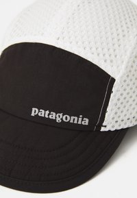 Svart og hvit mesh trucker cap med buet skjerm og "Patagonia"-logo på frontpanelet.