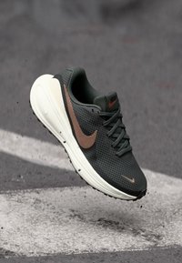 Dunkelgrüner Sportschuh mit strukturiertem Obermaterial, braunen Akzenten und einer weißen Sohle. Verfügt über eine Schnürung und ein großes Nike-Swoosh-Logo.