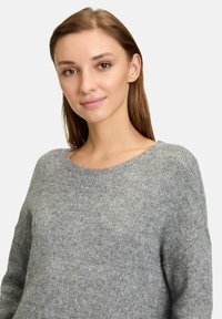 Pull gris en tricot avec un large décolleté et des manches longues, offrant une texture douce et une coupe légèrement ample.