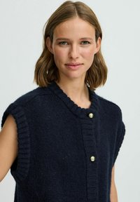 Marineblaue, gestrickte ärmellose Weste mit geripptem Kragen und Vorderseite, ausgestattet mit runden goldfarbenen Knöpfen und einem weichen, strukturierten Stoff.