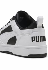 Hvide og sorte atletiske sneakers med overdel i syntetisk læder, struktureret gummisål og fremtrædende "PUMA"-branding bagpå.