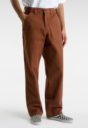 Pantaloni di cotone marroni con taglio dritto, tasche frontali e chiusura con un solo bottone, abbinati a scarpe slip-on a scacchi bianchi e neri.