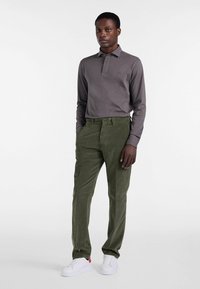 Długosleeve szary polo zestawiony z zielonymi spodniami z korduroju i białymi trampkami z czerwonymi akcentami, stojąc na jednolitym tle.