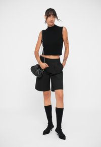Mustas varrukateta crop-top, kohandatud mustad lühikesed püksid, põlvepikkused mustad sokid ja terava ninaga mustad kontsad. Omab väikest musta kotti ketiga.