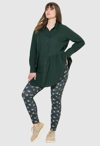 Groen lang knopen-overhemd met een gathering in de taille, gecombineerd met patroonleggings in donkere tinten en beige sneakers. Gevoerde stofaccenten.