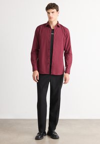 Bordeaux knaptrykt skjorte med lange ærmer, parret med sorte lige ben bukser og sorte sko, der skaber et formelt look. Glat stoftekstur.