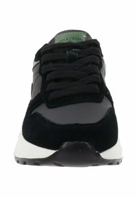 Zapatilla negra que presenta una combinación de materiales sintéticos suaves y gamuza texturizada, con una suela blanca y un acento verde en la lengüeta.