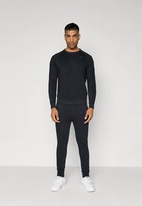 Sudadera negra y pantalones joggers a juego hechos de tela suave, con un diseño ajustado y puños acanalados. Zapatillas deportivas blancas completan el conjunto.