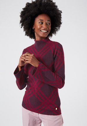 Dichtsluitende bordeauxrode turtleneck trui met ribbelstructuur en contrasterend rood ruitpatroon. Kenmerkt zich door klokvormige mouwen en een klein accentlogo.