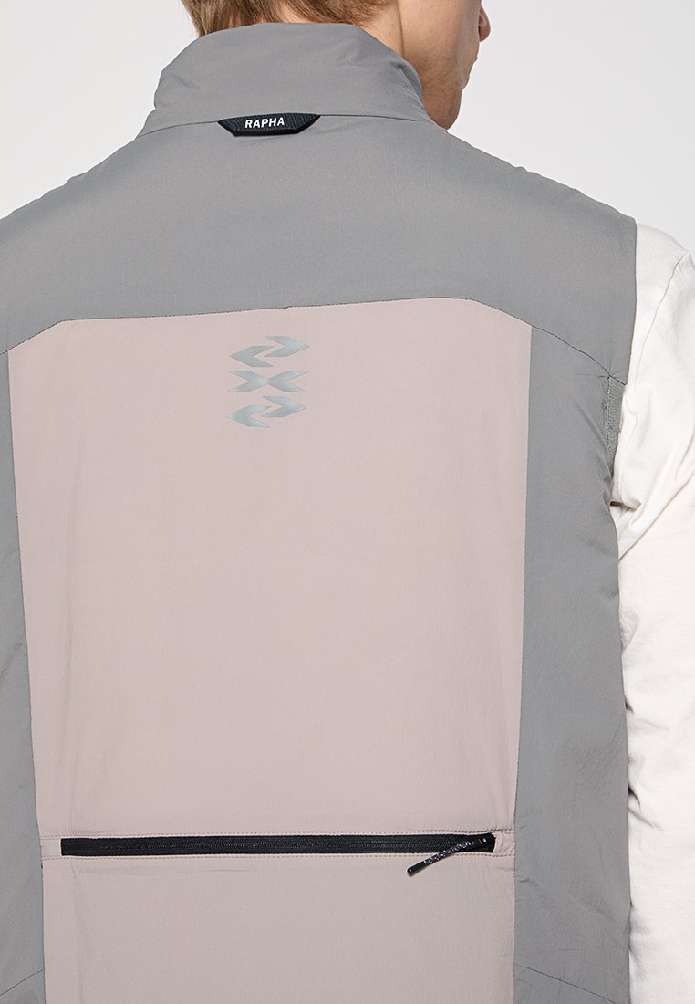Graue und hellrosa ärmellose Jacke mit hohem Kragen, rückseitiger Reißverschlusstasche und Rapha-Logo. Sie verfügt über glattes Material und ein schlankes Design.