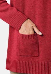 Roter, gestrickter Pullover mit gerippten Bündchen und Saum. Verfügt über eine Tasche auf der Vorderseite. Der strukturierte Stoff wirkt weich und warm.