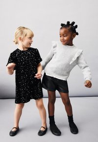 Černé šaty s flitry a krátkými rukávy vlevo; šedý svetr s volánky vpravo, doplněný černými šortkami a botami.