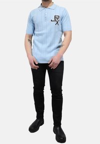 Světle modrá pletená polo košile s límečkem, krátkými rukávy, vertikálními pruhy a černým logem na hrudi; spárována s černými slim-fit džíny a černými botami.