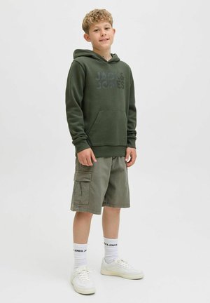 Sudadera verde con bolsillo frontal y logo negro, combinada con pantalones cortos de carga verdes claros, zapatillas blancas y calcetines con logo. Fondo neutro.
