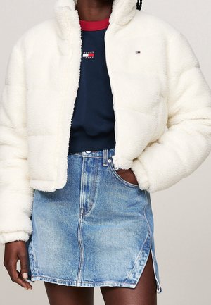 Personne portant une veste blanche duveteuse par-dessus un sweat-shirt Tommy Jeans bleu marine et une jupe en denim bleu clair avec une fente à l'avant.