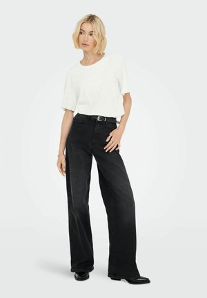 Hvid kortærmet t-shirt parret med højtaljede sorte brede jeans. Jeansene har en lige pasform og mørk vask, båret med sorte støvler.