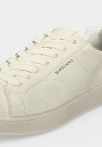 Baskets blanches Björn Borg avec lacets, coutures visibles et nom de la marque imprimé sur le côté, présentées sur un fond uni.