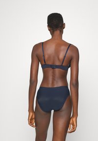 Navy blue bikini set, featuring a smooth texture, adjustable straps, and a clasp closure on the back of the top and high-waisted bottom.
