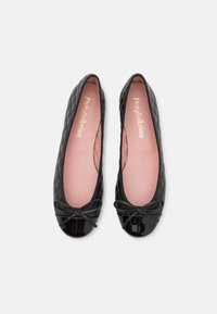Ballerines noires matelassées avec un bout glossy et un accent en nœud. L'intérieur présente une doublure rose douce et un marquage doré.