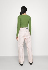 Zelený rebrovaný top s dlouhým rukávem spárovaný s růžovými kostkovanými kalhotami. Kalhoty mají cedulku na pasu s nápisem "RAGGED." Černé platformové boty.