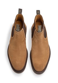Paired de bottines Chelsea en daim beige avec panneaux latéraux élastiques foncés et semelles cousues marron, vues de dessus sur un fond blanc.
