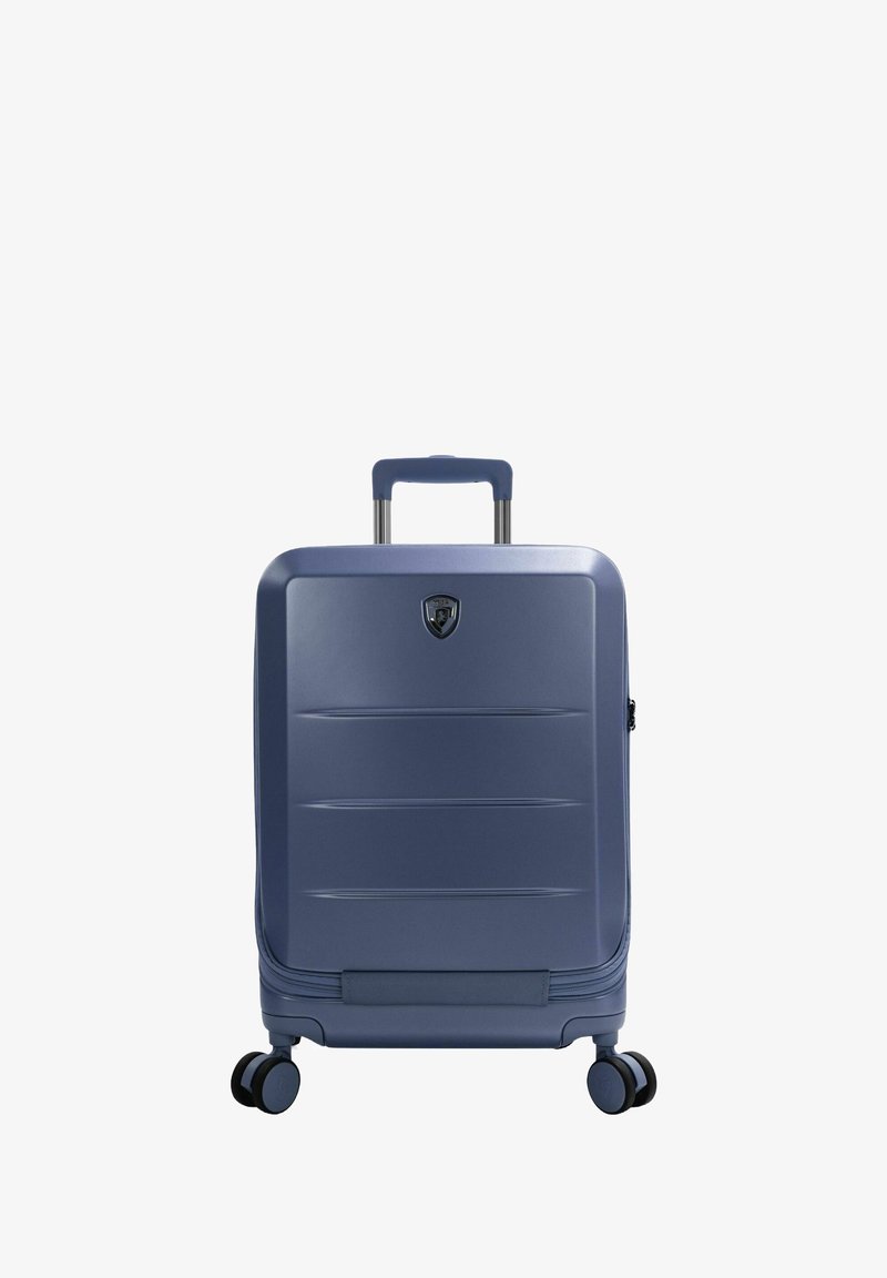 Valigia rigida blu navy con texture liscia, scanalature verticali, manico telescopico e quattro ruote girevoli per una facile mobilità.
