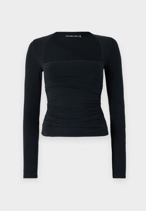 Camisa preta de manga longa feita de tecido macio, com um design justo e detalhe franzido na cintura, além de painéis de ombros sem emendas em contraste.