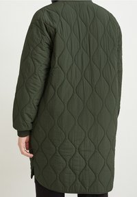 Quilted long coat in dark green, featuring a wavy pattern and a relaxed fit. The sleeves end with black ribbed cuffs. Textured fabric.