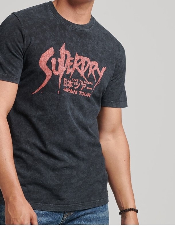 Camiseta gráfica negra con un acabado desgastado, que presenta letras rojas para "Superdry" y "Japan Tour". Cuello redondo clásico y mangas cortas.