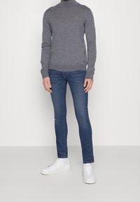 Harmaa poolopaita yhdistettynä tummansinisiin farkkuihin ja valkoisiin tennareihin. Paita on muotoilultaan slim fit ja siinä on ribbaatut hihansuut ja helma.