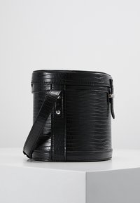 Musta pyöreä laukku krokotiilinkuosilla, vetoketjusuljenta ja irrotettava hihna. Ominaisuuksiin kuuluu sileä pinta ja yksivärinen muotoilu.