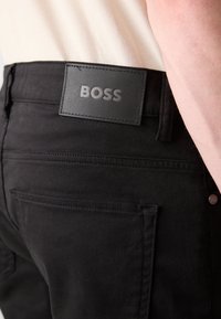 Zwarte denim broek met een gestructureerde afwerking, logo-label op de tailleband en achterzakken met gestikte details.