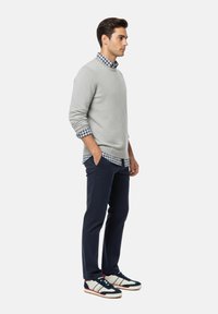 Suéter de punto gris sobre una camisa a cuadros azul y blanca, combinado con pantalones navy y zapatillas blancas con acentos en azul y rojo.