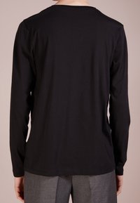 Schwarzes Langarm-T-Shirt aus Baumwolle mit Rundhalsausschnitt und glatter Textur, von hinten vor einem neutralen Hintergrund gezeigt.