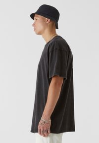 Oversized black cotton t-shirt with a round neck, short sleeves, and minimalistic design. A black bucket hat completes the look.