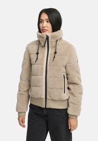 Beige fleece pufferjack met hoge kraag, zwarte rits en trekkoorden. Kenmerkt zich door een horizontaal gewatteerd patroon en ribbels aan de mouwen.