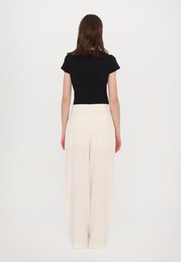 Zwart top met korte mouwen in combinatie met hoog-waisted, wijde broek in crème. Soepele stof met een schoon, minimalistisch ontwerp.