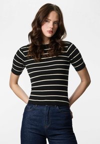 Crno-bijela prugasta rebrasta majica s kratkim rukavima i okruglim izrezom, uparena s tamnoplavim trapericama s visokim strukom.