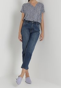 Modrá květinová blůza s krátkým rukávem, modré džíny s vysokým pasem a světle levandulové muly s kontrastními tmavými akcenty. Hladké textury látek.