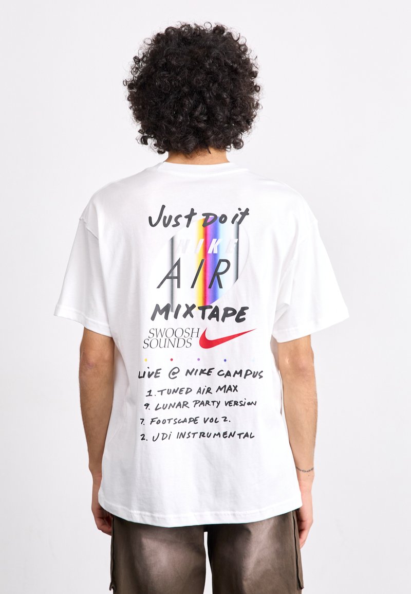Balta medvilninė marškinėlių su trumpomis rankovėmis, turinti spalvingą grafikos dizainą nugaros pusėje su užrašais, įskaitant "Tiesiog padaryk tai", "NIKE AIR" ir mixtape takelių sąrašą.