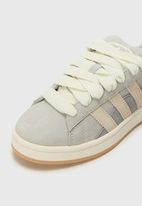 Baskets en daim gris clair avec des rayures beige, des lacets épais crème et une semelle blanche avec une semelle couleur gomme.
