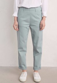 Pantalons taille haute vert clair en mélange de coton, avec des ourlets roulés, des plis à l'avant et deux boutons latéraux à la taille.